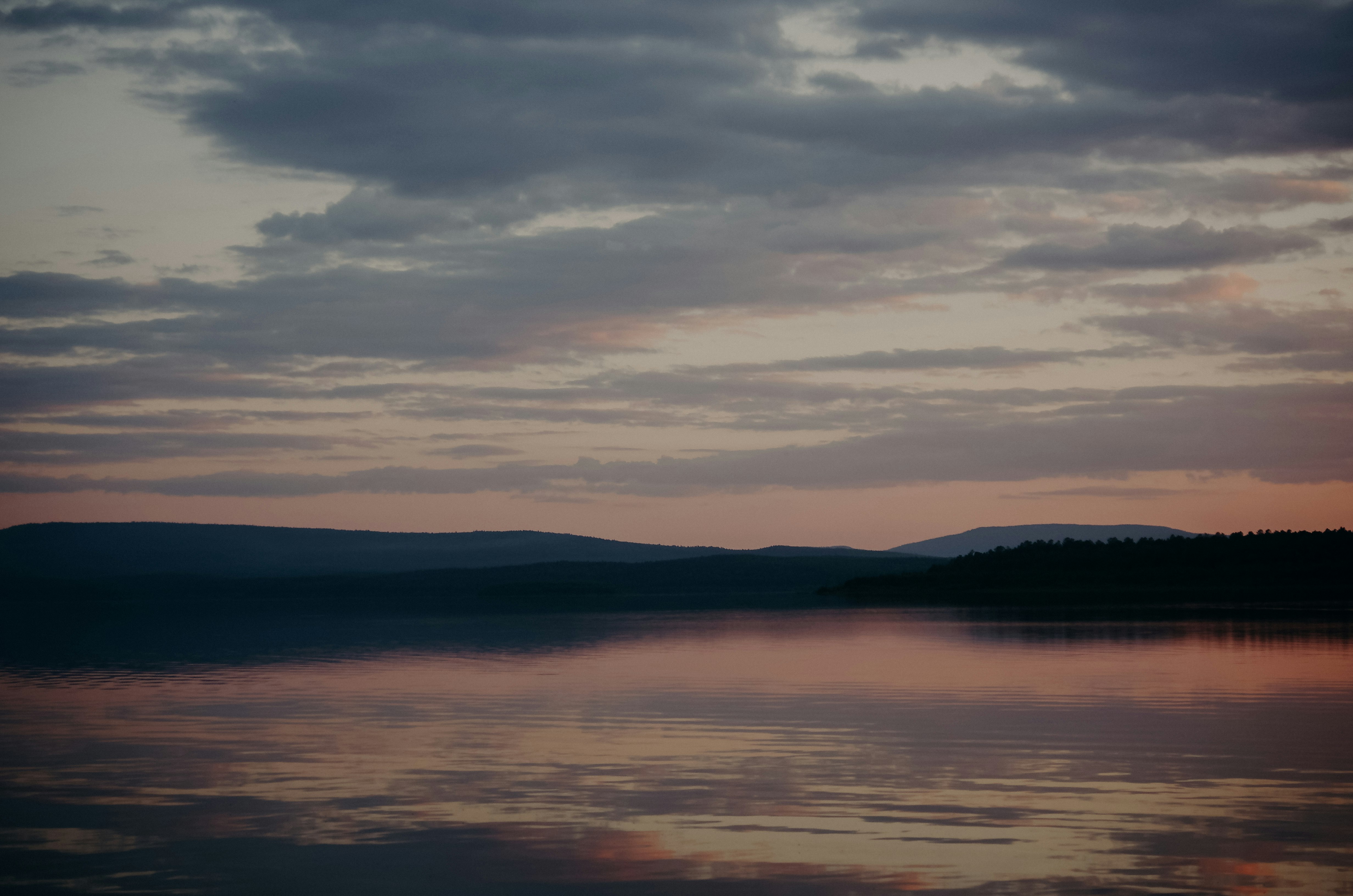 body of water near mountain during sunset