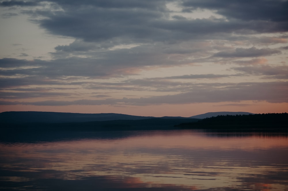 body of water near mountain during sunset