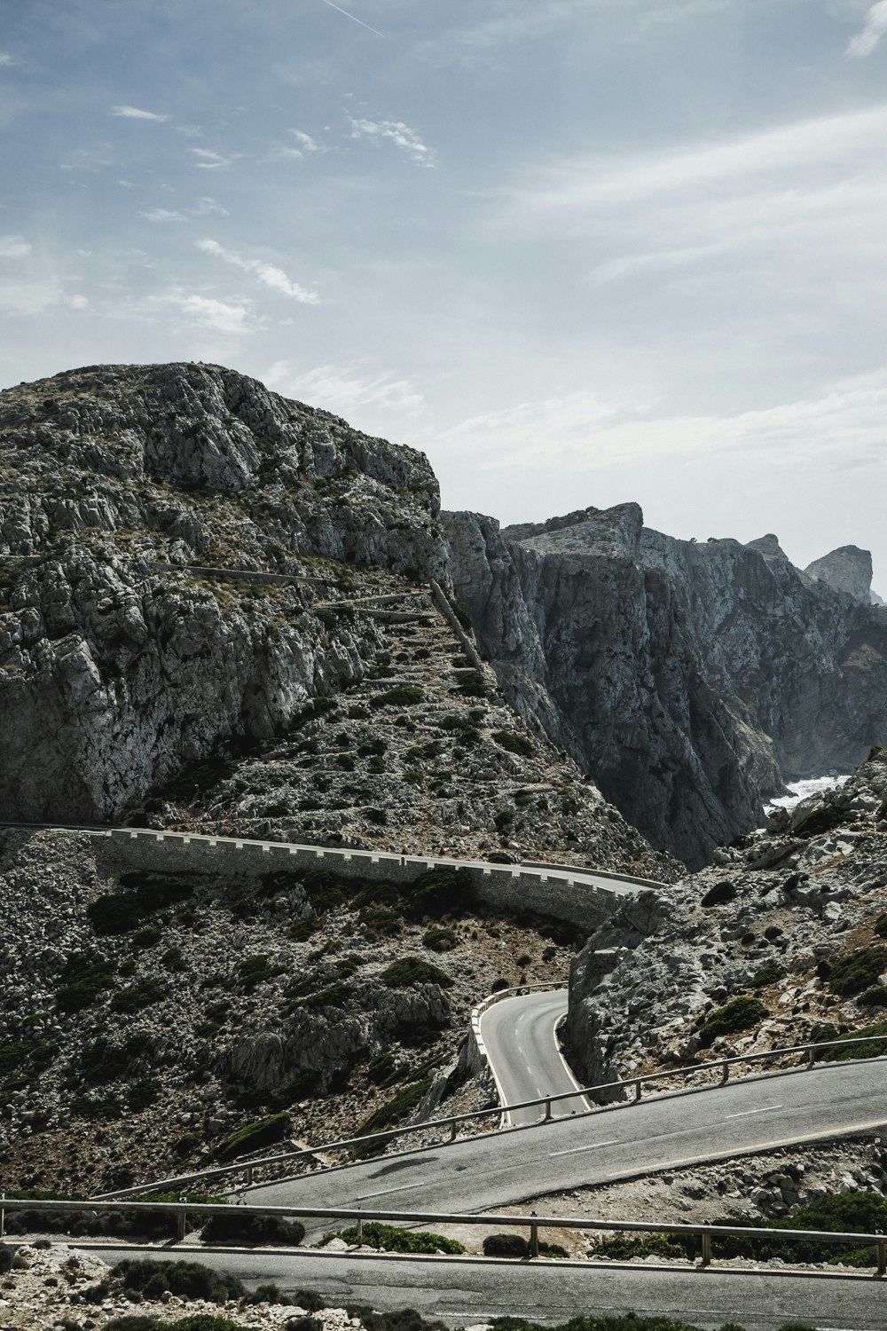 gray concrete road between rocky mountains under white cloudy sky during daytime