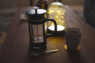 Tasse en céramique blanche à côté d'une presse à café noire sur une table en bois brun