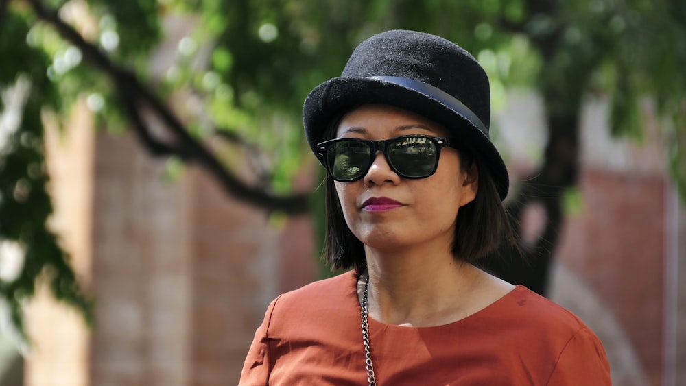 woman in orange crew neck shirt wearing black fedora hat and black sunglasses