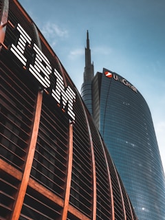 Two prominent skyscrapers with one building featuring a wooden panel design and the IBM logo, while the other shows the UniCredit logo on a sleek glass facade. The sky is clear with a few clouds, creating a modern and corporate atmosphere.