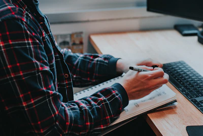 person in red black and white plaid long sleeve shirt writing on white paper