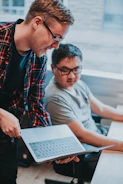 A professional setting showing a manager guiding a new employee through onboarding tasks on a laptop.