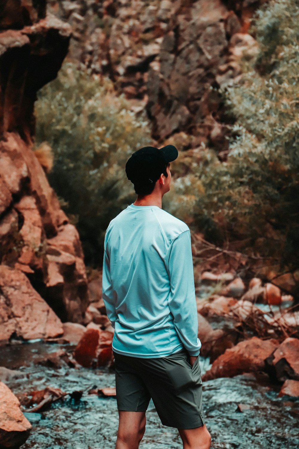 man in blue shirt and black cap standing in front of brown rock formation during daytime