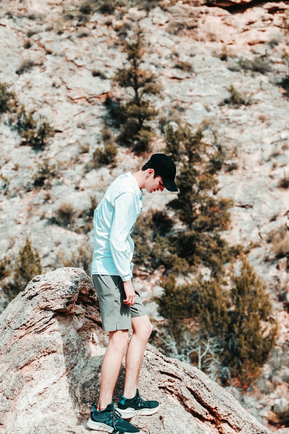 man in white dress shirt and brown shorts standing on brown rock during daytime