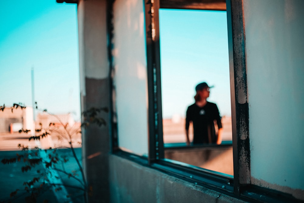 man in black shirt standing beside window during daytime