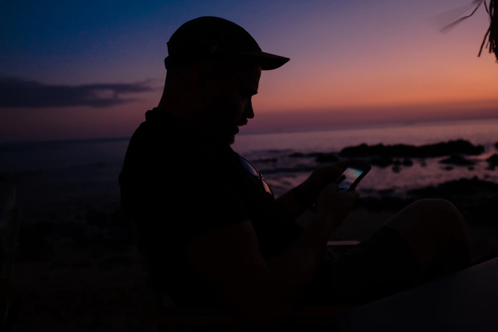 Silhouette of a traveller checking a phone on the shore at dusk, with the hotspot turned off to save battery
