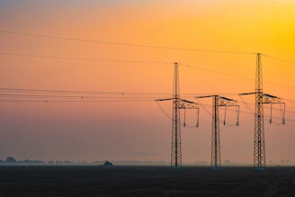 A panoramic view of a modern electrical substation at sunset with glowing power lines.