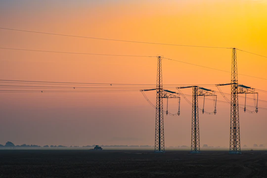 A panoramic view of a modern electrical substation at sunset with glowing power lines.
