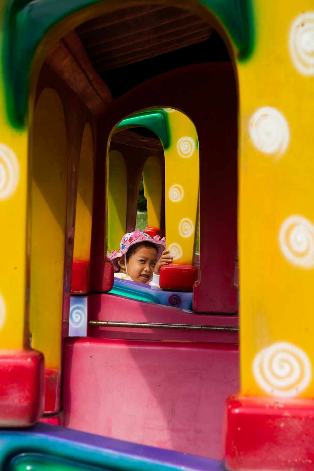 girl in pink jacket sitting on red and yellow slide