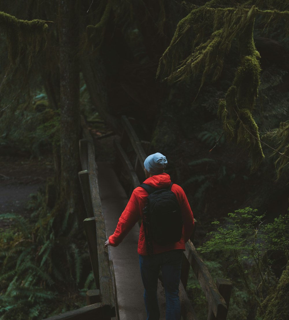 man in red jacket and black pants wearing white helmet standing on brown wooden bridge during