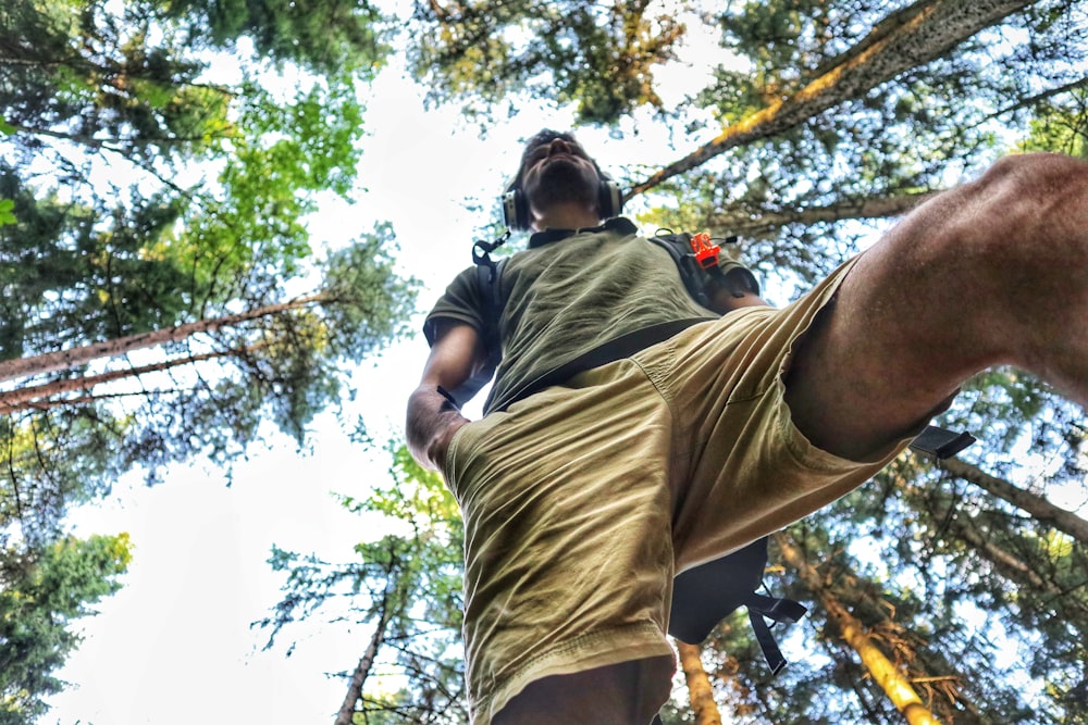 man in green t-shirt and brown pants climbing on brown tree during daytime