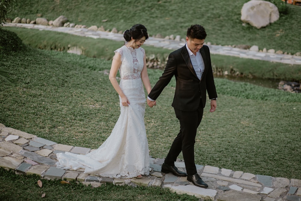 man in black suit and woman in white wedding dress walking on green grass field during