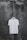 A plain white T-shirt hangs on a wooden hanger against a textured, dark, weathered concrete wall.