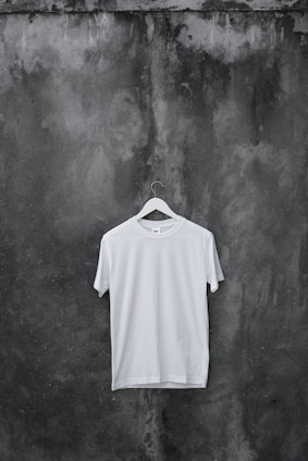 A plain white t-shirt hanging on a wooden hanger against a neutral background