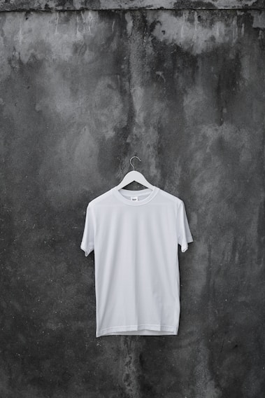 Men's casual t-shirt hanging on a rustic wooden hanger against a bright urban backdrop.