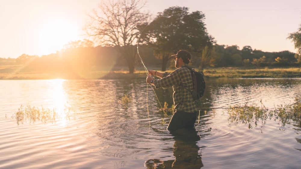 man in black and white plaid dress shirt fishing on lake during daytime