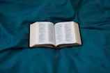 An open book with pages tinted in soft teal and peach hues, resting on a wooden table.