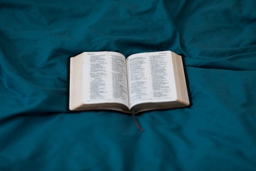 An open book with pages tinted in soft teal and peach hues, resting on a wooden table.