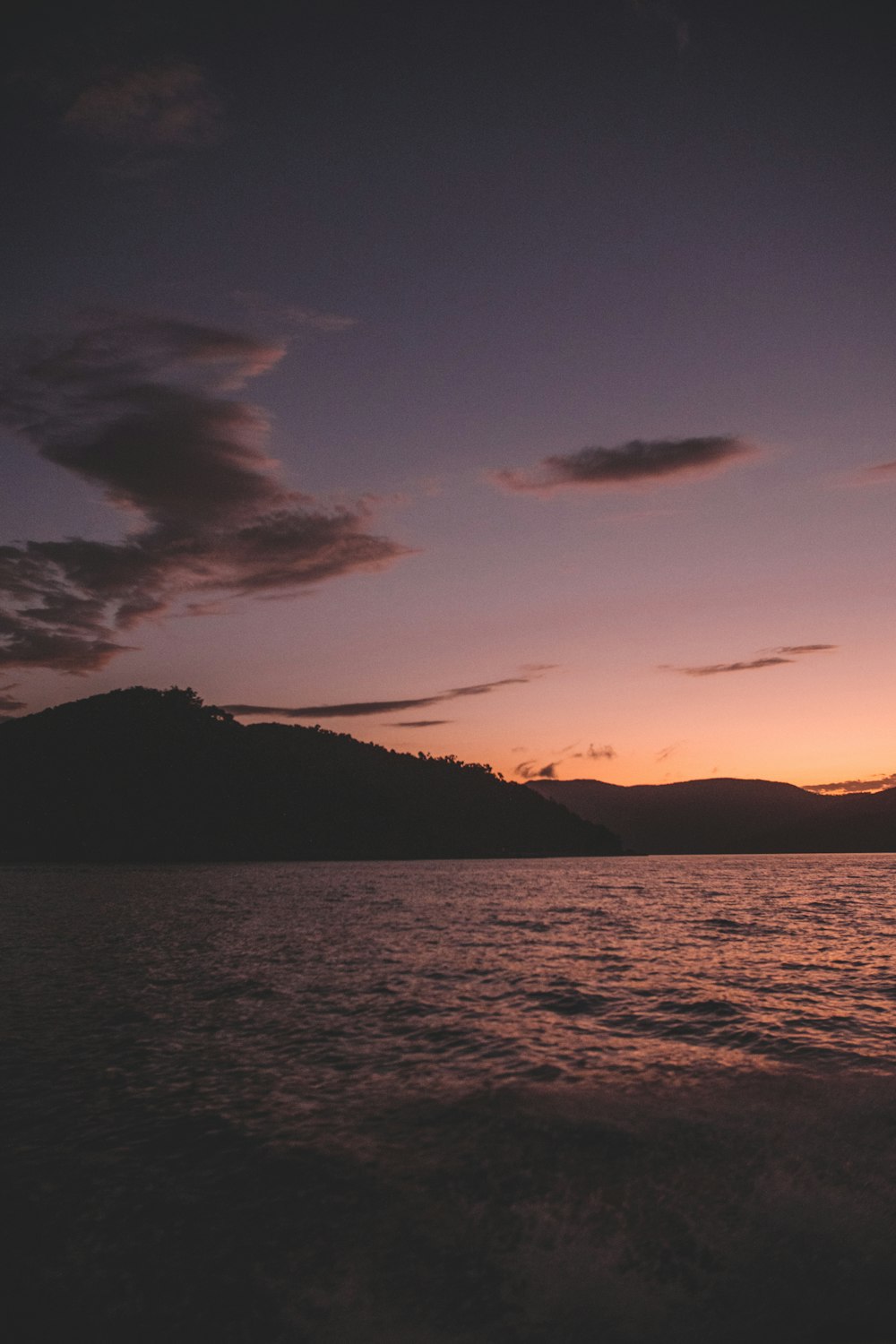 silhouette of mountain near body of water during sunset