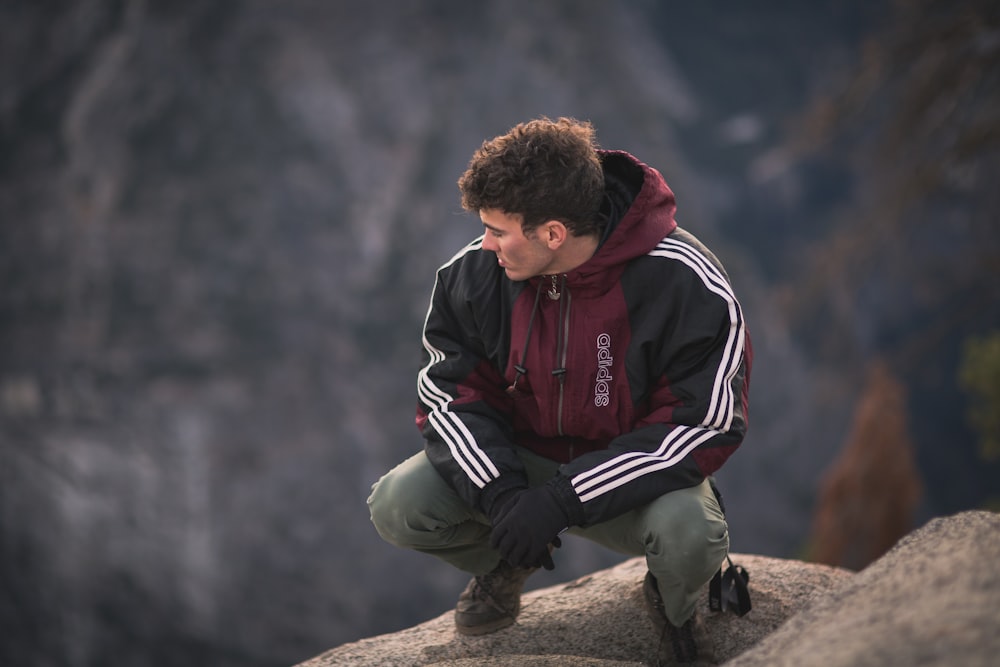 岩の上に座る赤と黒のジャケットを着た男