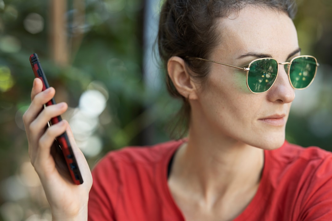 woman in red crew neck shirt wearing green sunglasses holding smartphone during daytime