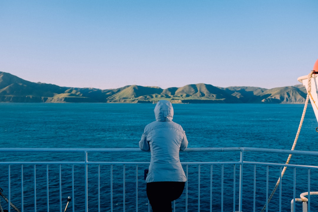 person in white hoodie standing on white metal railings near body of water during daytime