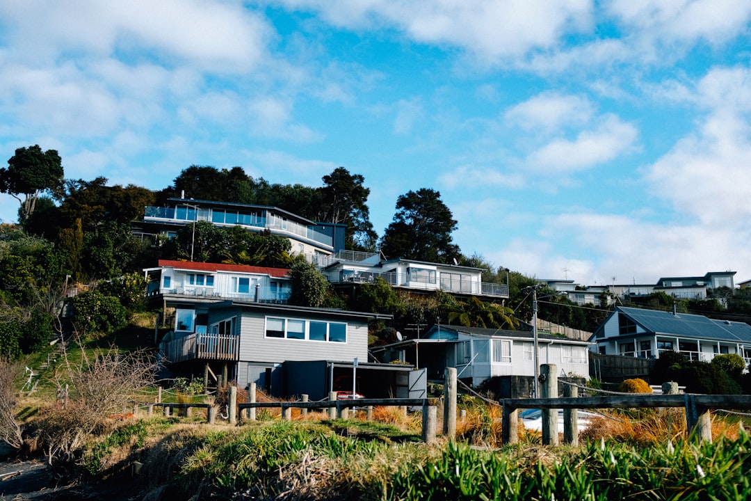 white and brown concrete house near green trees under white clouds during daytime