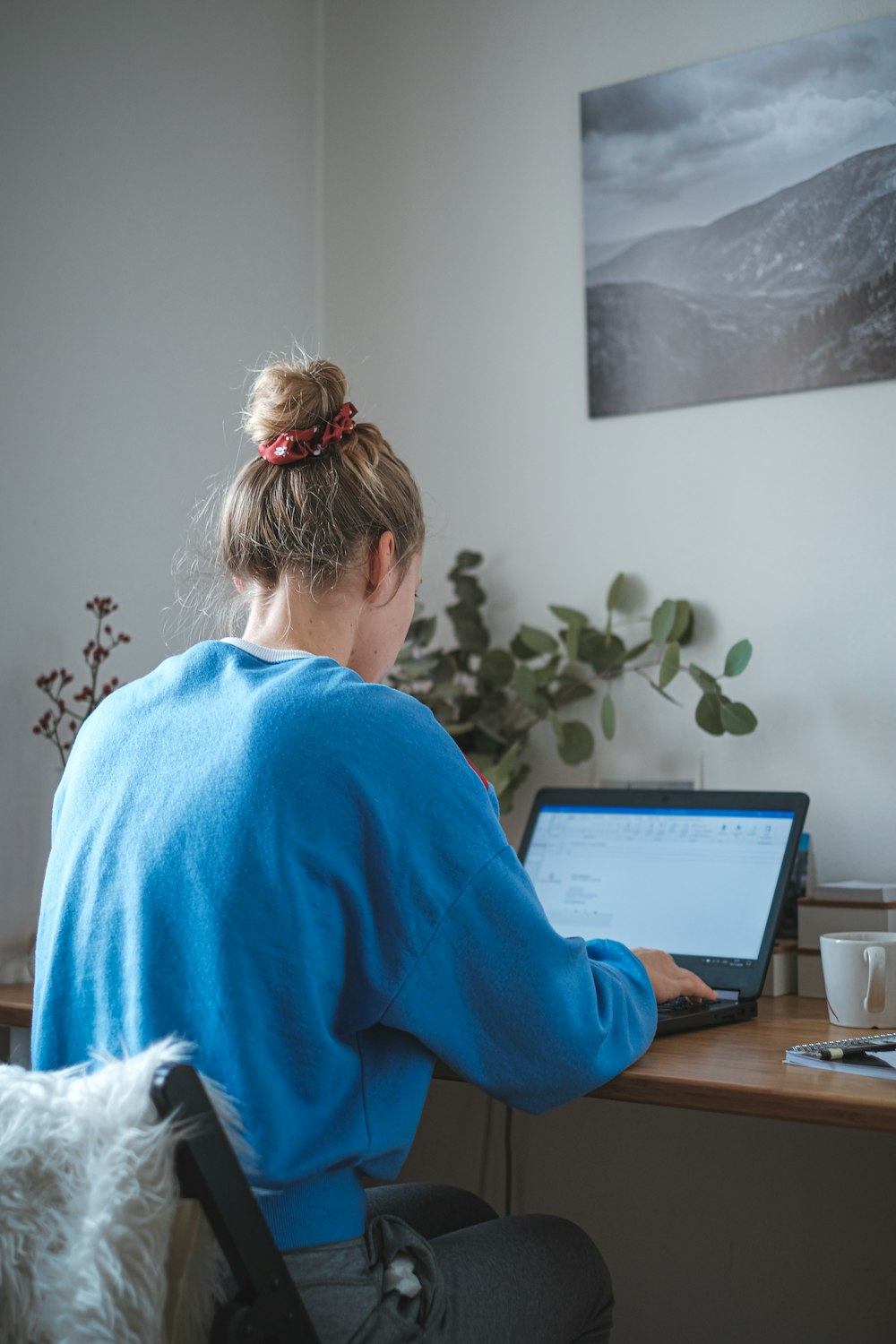 노트북 컴퓨터 앞에 앉아 있는 파란색 스웨터를 입은 여자