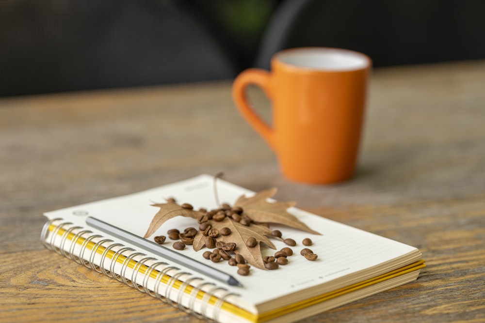 white book beside orange ceramic mug on brown wooden table