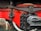A close-up view of a mechanical component, possibly from a train or heavy machinery. It features a glossy red painted surface, black metal parts with visible bolts, and a textured finish. The detailed view showcases the intricate connections and engineering design.