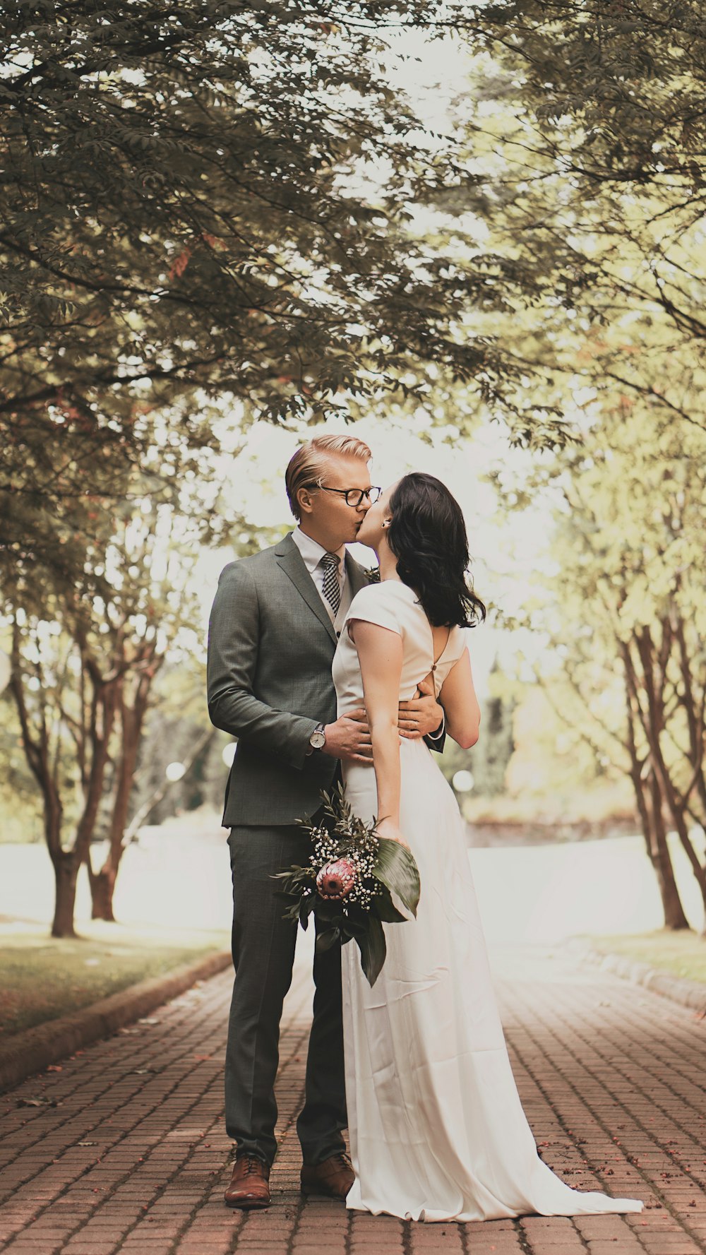 man in black suit jacket kissing woman in white wedding dress during daytime