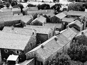 An aerial view of a historic European village nestled between rolling hills and winding roads.