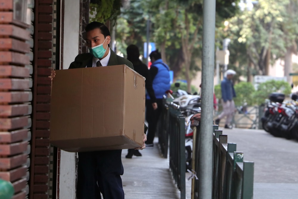 man in black jacket carrying brown cardboard box