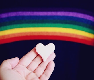 person holding white heart shaped ornament with rainbow above