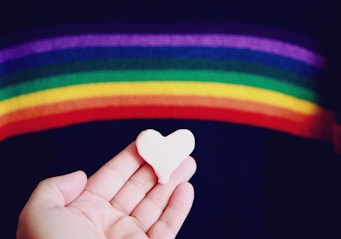 person holding white heart shaped ornament with rainbow above