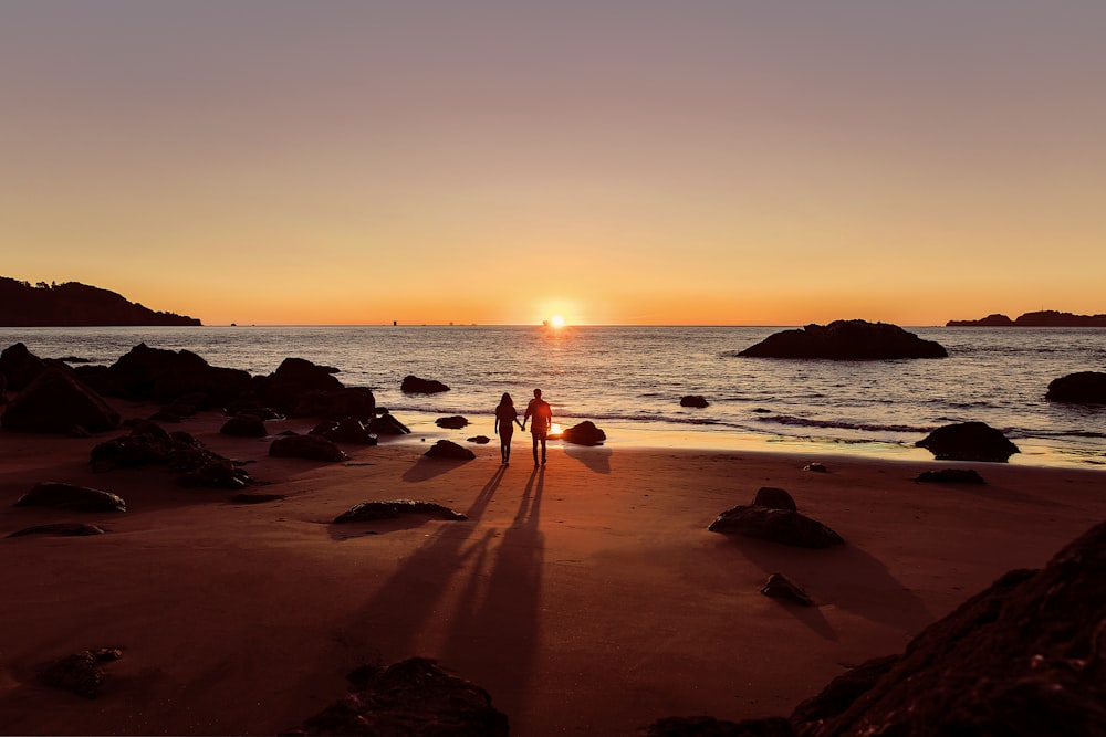 homem em shorts pretos andando na praia durante o pôr do sol