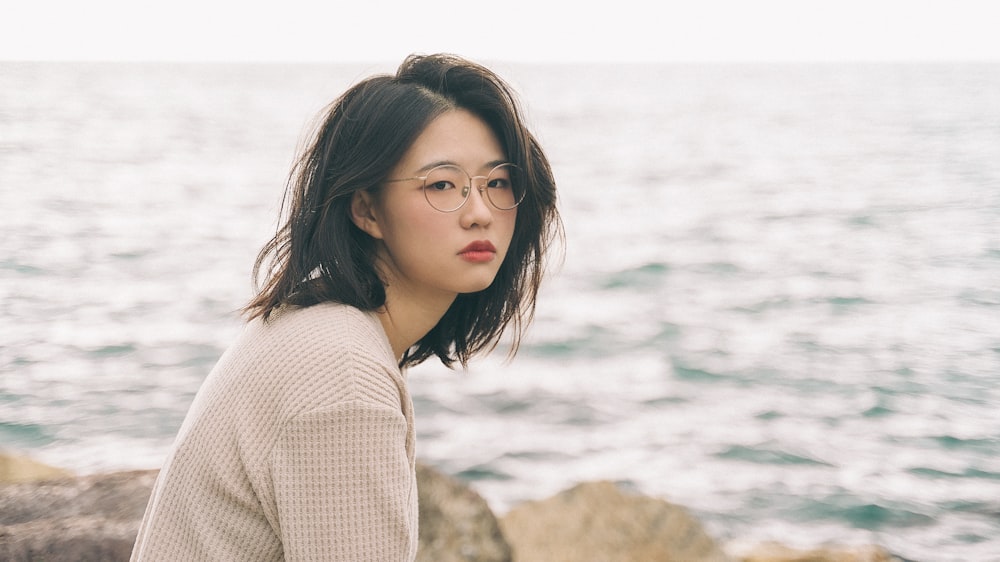 woman in white sweater standing on brown rock near body of water during daytime