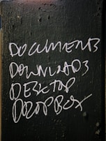 Handwritten white text on a dark green, textured surface lists the words: DOCUMENTS, DOWNLOADS, DESKTOP, and DROPBOX.