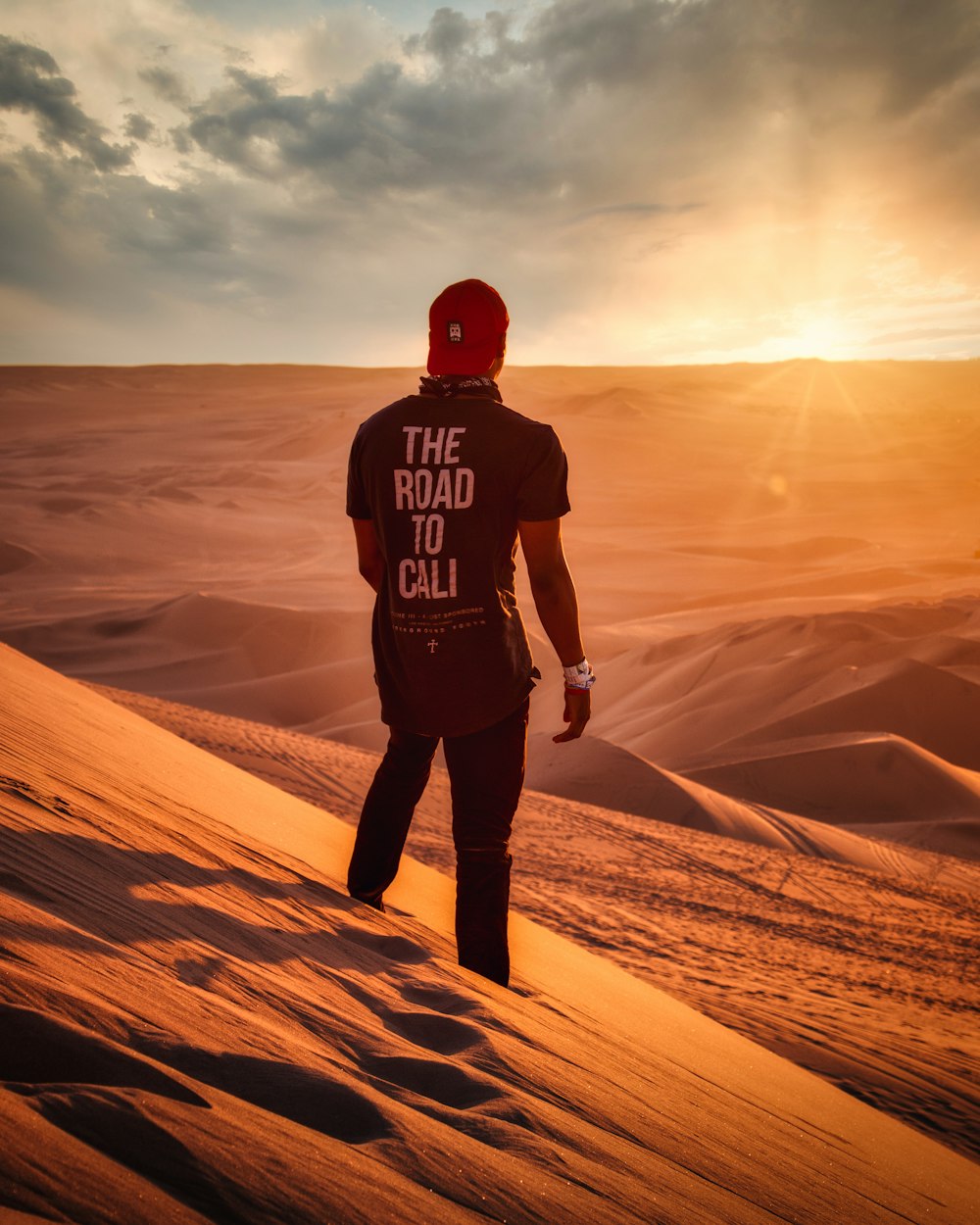 man in black and red hoodie standing on brown sand during daytime