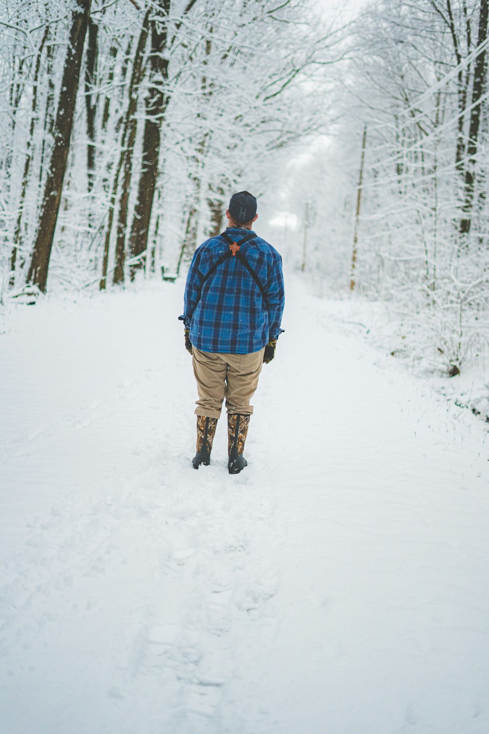 昼間、雪に覆われた地面を歩く青いジャケットと茶色のズボンを着た男性