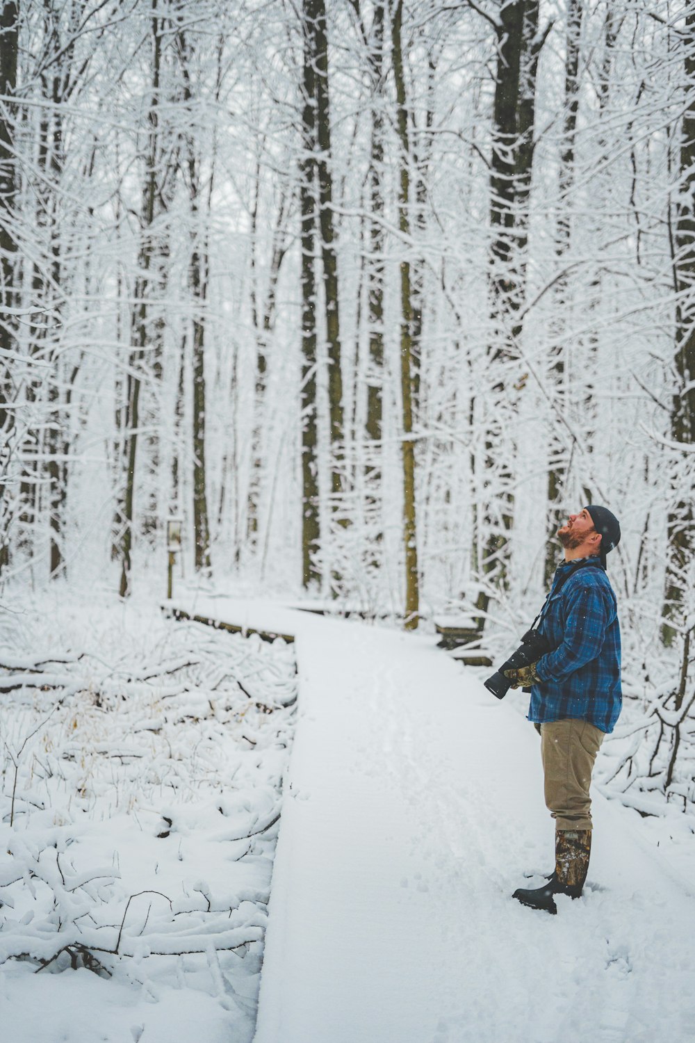 man in blue and black plaid dress shirt and brown pants walking on snow covered ground