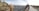 A panoramic view of a historical cityscape with ancient architectural structures featuring domes and intricate designs. A pathway leads along the edge of the buildings, with people walking and taking photos. The expansive city stretches into the distance under a partly cloudy sky.