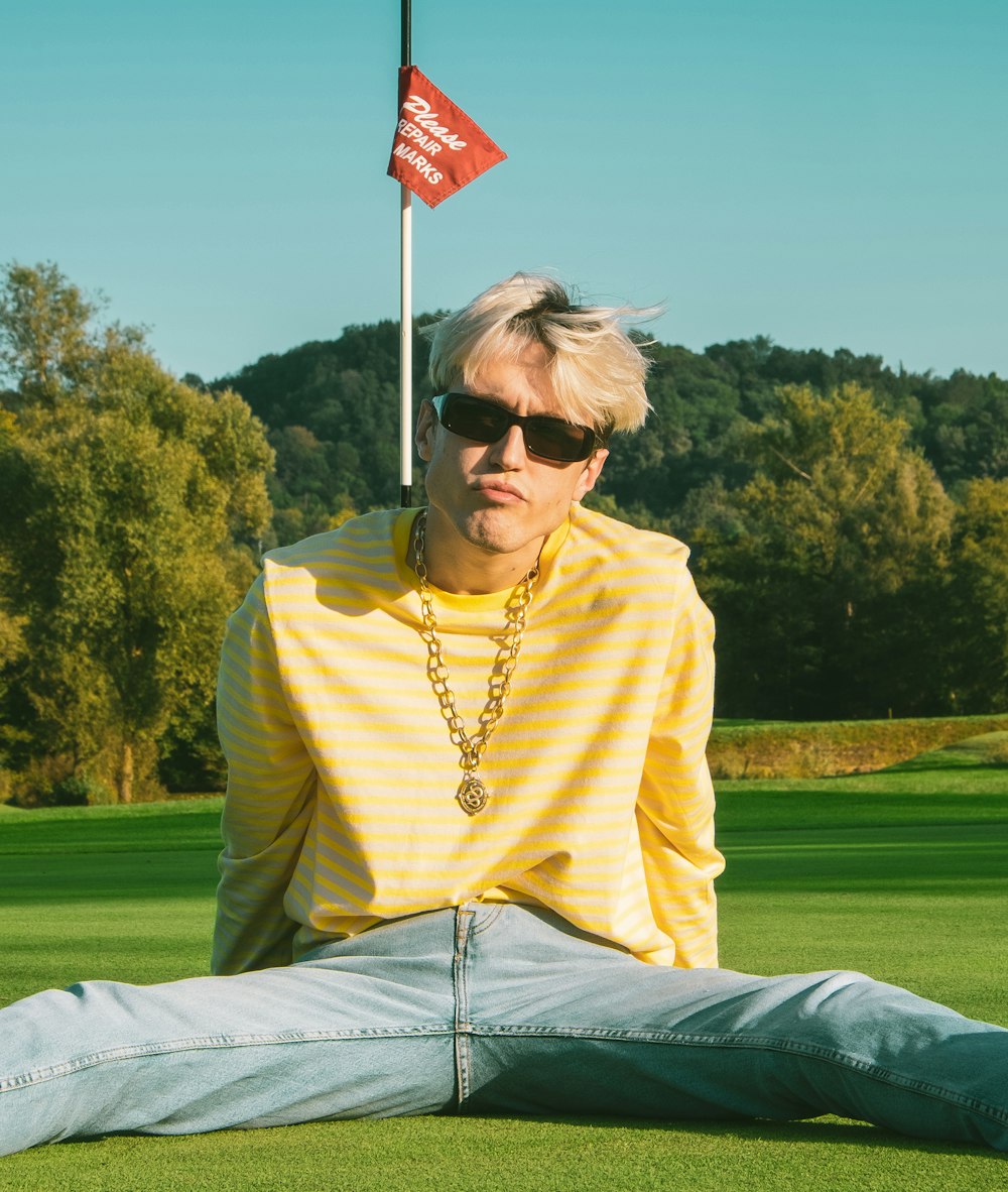 woman in yellow long sleeve shirt wearing black sunglasses sitting on green grass field during daytime