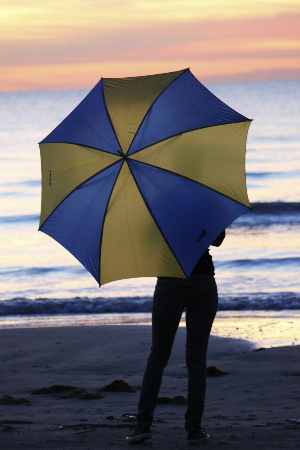 person in blue umbrella walking on beach during daytime