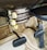 The image displays an old-fashioned car climate control system with dials labeled ‘DE-FOG,’ ‘DE-ICE,’ ‘LOW,’ ‘MED,’ ‘HI,’ ‘OFF,’ 'WARMER,' and levers marked ‘DEF,’ ‘AIR,’ ‘TEMP.’ The setup is situated above a carpeted floor and beneath a pair of foot pedals, typical of a classic vehicle interior.