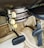 The image displays an old-fashioned car climate control system with dials labeled ‘DE-FOG,’ ‘DE-ICE,’ ‘LOW,’ ‘MED,’ ‘HI,’ ‘OFF,’ 'WARMER,' and levers marked ‘DEF,’ ‘AIR,’ ‘TEMP.’ The setup is situated above a carpeted floor and beneath a pair of foot pedals, typical of a classic vehicle interior.