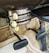 The image displays an old-fashioned car climate control system with dials labeled ‘DE-FOG,’ ‘DE-ICE,’ ‘LOW,’ ‘MED,’ ‘HI,’ ‘OFF,’ 'WARMER,' and levers marked ‘DEF,’ ‘AIR,’ ‘TEMP.’ The setup is situated above a carpeted floor and beneath a pair of foot pedals, typical of a classic vehicle interior.