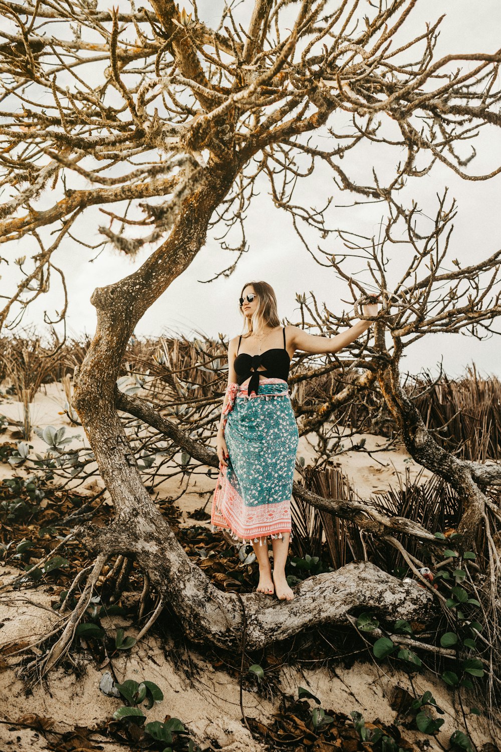 Muchacha en vestido floral rosa y blanco de pie junto al árbol marrón